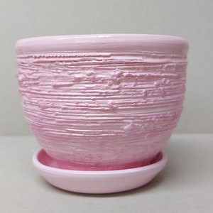 Puede incluir: Una maceta de cerámica rosa con un diseño texturizado a rayas. La maceta tiene un platillo a juego.
