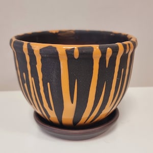May include: A ceramic planter with a black and orange striped design. The planter has a matching saucer.