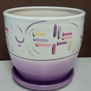 May include: A white ceramic planter with a purple ombre design and a matching saucer. The planter features a geometric pattern in pink, yellow, and purple.