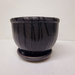 Peut inclure: Un pot de fleur en céramique brun foncé avec une soucoupe assortie. Le pot a une forme arrondie avec des rainures verticales et une finition brillante. La soucoupe est un disque plat simple. Idéal pour les plantes.