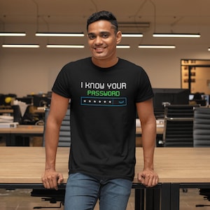 Op de afbeelding: Een zwart T-shirt met de tekst "I know your password" in groene en blauwe letters. De tekst wordt gevolgd door een rij van vijf sterren en een symbool dat lijkt op een gesloten oog.