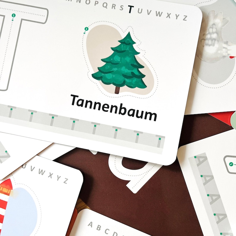 K&ouml;nnte beinhalten: Eine wei&szlig;e Lernkarte mit dem Buchstaben T, einer Illustration eines gr&uuml;nen Tannenbaums und dem in Schwarz gedruckten Wort Tannenbaum. Die Karte enth&auml;lt ein gepunktetes T zum Nachspuren, eine Buchstabenfolge und eine untere Reihe gr&uuml;ner Punkte.