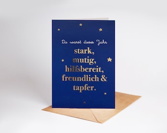 May include: A blue card with gold foil lettering that reads "Du warst dieses Jahr stark, mutig, hilfsbereit, freundlich & tapfer."  The card is decorated with gold stars.