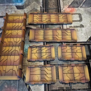 May include: A collection of modular, brown and yellow terrain pieces for tabletop gaming. The set includes various wall and barrier components with geometric designs, ideal for creating a sci-fi or industrial setting.