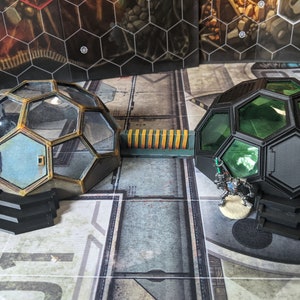 May include: Two futuristic, dome-shaped structures with black and gold accents. The domes have clear and green glass panels. A small, silver robot figure stands in front of the green dome.