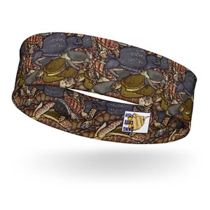 Könnte beinhalten: Ein braunes Stirnband mit einem sich wiederholenden Muster von Meeresschildkröten. Das Stirnband hat ein kleines Logo an der Seite, auf dem "Dang Cute Fish" steht.