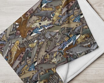 May include: A soft, plush fleece blanket featuring a colorful pattern of various fish, including sharks, rays, and other marine life. The blanket is white on the reverse side.