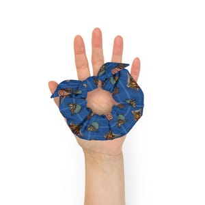 May include: A blue scrunchie with a white and brown pattern of small sea creatures. The scrunchie is tied in a knot and held in a hand.