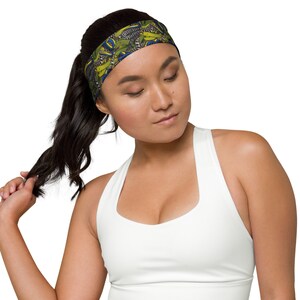 May include: A woman with long dark hair is wearing a white tank top and a patterned headband. The headband has a green, yellow, blue, and black pattern.