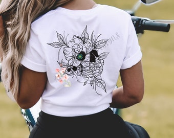 May include: White t-shirt with a black and white floral skull design on the back. The skull is surrounded by flowers and leaves. There is a small cluster of pink flowers on the left side of the skull.