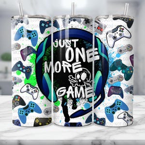 May include: A white tumbler with a blue and green design featuring a skull and crossbones and the text "Just One More Game". The tumbler is surrounded by images of video game controllers.