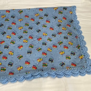 May include: A blue baby blanket with a crocheted border. The blanket features a repeating pattern of colorful toy trains on a light blue background.