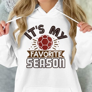 以下が含まれることがあります： 中央にサッカーボールが描かれた、"It's My Favorite Season"と書いてある茶色のグラフィックが施された白いパーカー