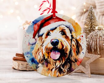 Peut inclure: Une peinture à l'aquarelle d'un chien portant un chapeau de Père Noël. Le chien est un doodle avec une fourrure brune et blanche. La peinture est sur une boule de Noël ronde en céramique blanche.