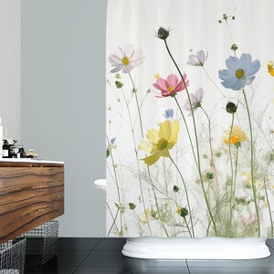 May include: A white shower curtain with a floral print featuring pressed flowers in shades of pink, yellow, blue, and white. The flowers are arranged in a random pattern on a white background.