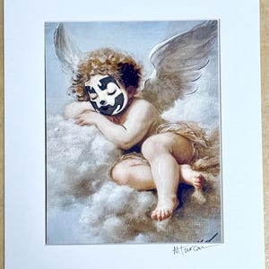 May include: A framed print featuring a cherubic figure with wings, resting on a cloud. The figure has curly brown hair and a black and white face mask. The artwork is signed in the lower right corner.