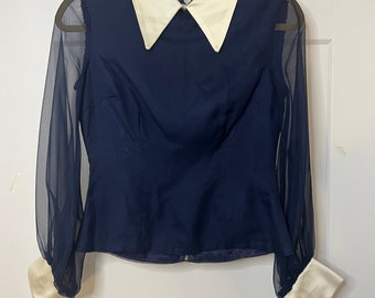 May include: A navy blue blouse with a white satin collar and sheer sleeves. The sleeves have white satin cuffs.