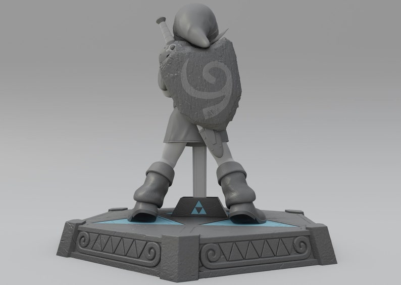 May include: A gray plastic figurine of Link from the Legend of Zelda video game series. Link is wearing a green tunic and holding a sword and shield. The figurine is standing on a gray base with a Triforce symbol.