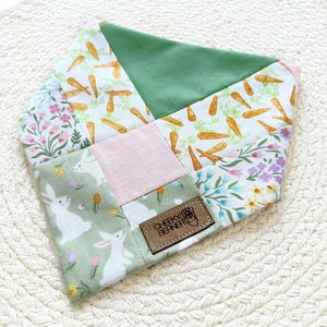May include: A green, pink and white patchwork bandana with a bunny and carrot print. The bandana has a brown leather tag that says "Cheeky Berner".