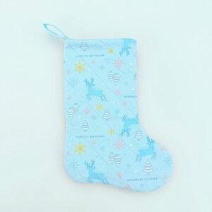 Peut inclure: Chaussette de Noël bleu clair avec un motif de rennes, de flocons de neige et d'arbres. Le texte "EXPECTO PATRONUM" est imprimé sur la chaussette. Elle a une boucle bleue pour l'accrocher.
