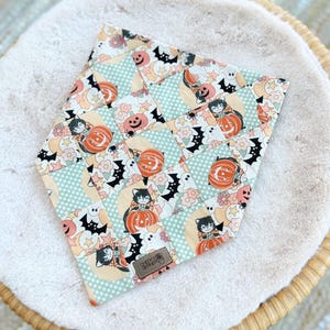 Peut inclure: Un bandana à motif patchwork vert, orange et noir avec des citrouilles, des chauves-souris, des fantômes et des chats. Le bandana a une étiquette en cuir marron avec le texte "Cheeky Pup Designs".