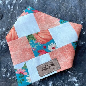 Peut inclure: Un bandana pour chien en patchwork avec un motif de patchwork dans les tons turquoise, blanc et p&ecirc;che. Le bandana pr&eacute;sente un imprim&eacute; de citrouille et un motif floral. Le bandana a une &eacute;tiquette en cuir marron avec le texte "CHEEKY BERNER".
