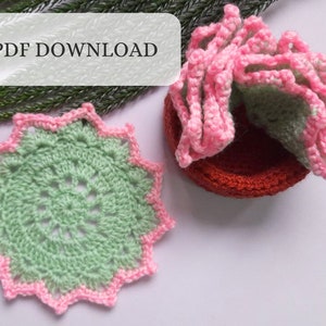 May include: A green and pink crocheted coaster with a starburst design. The coaster is on a white surface. PDF DOWNLOAD is written on a white rectangle.