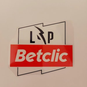 Può includere: Un adesivo con sfondo bianco e contorno nero. L'adesivo presenta il testo "L P" in nero, con un fulmine. Sotto c'è un rettangolo rosso con la parola "Betclic" in bianco.