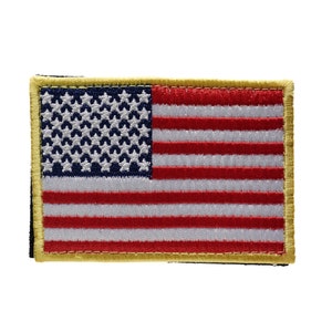 Può includere: Un piccolo patch ricamato della bandiera americana con un bordo dorato. La bandiera è rossa, bianca e blu con 13 strisce e 50 stelle.