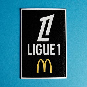 Può includere: Toppa bianca e nera con il numero "1" e il testo "LIGUE 1" in bianco. Un logo "M" giallo si trova sotto il testo.