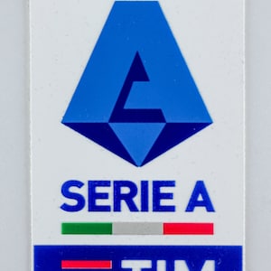 Puede incluir: Una pegatina rectangular con el logotipo de la Serie A para la temporada 2023-2024. El diseño incluye una 'A' geométrica azul, las palabras 'SERIE A' y el logotipo de TIM. También están presentes los colores de la bandera italiana.