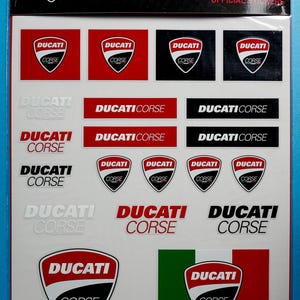 May include: A sheet of official Ducati Corse stickers featuring various logos and designs. The stickers are white, red, black, and grey with the Ducati Corse logo in different sizes and styles.