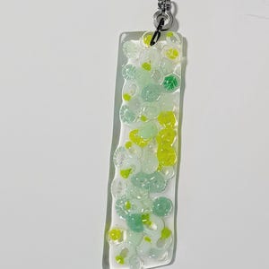 May include: A rectangular, clear glass light pull with a pattern of green and yellow fused glass circles. The pull is attached to a silver-colored ball chain.