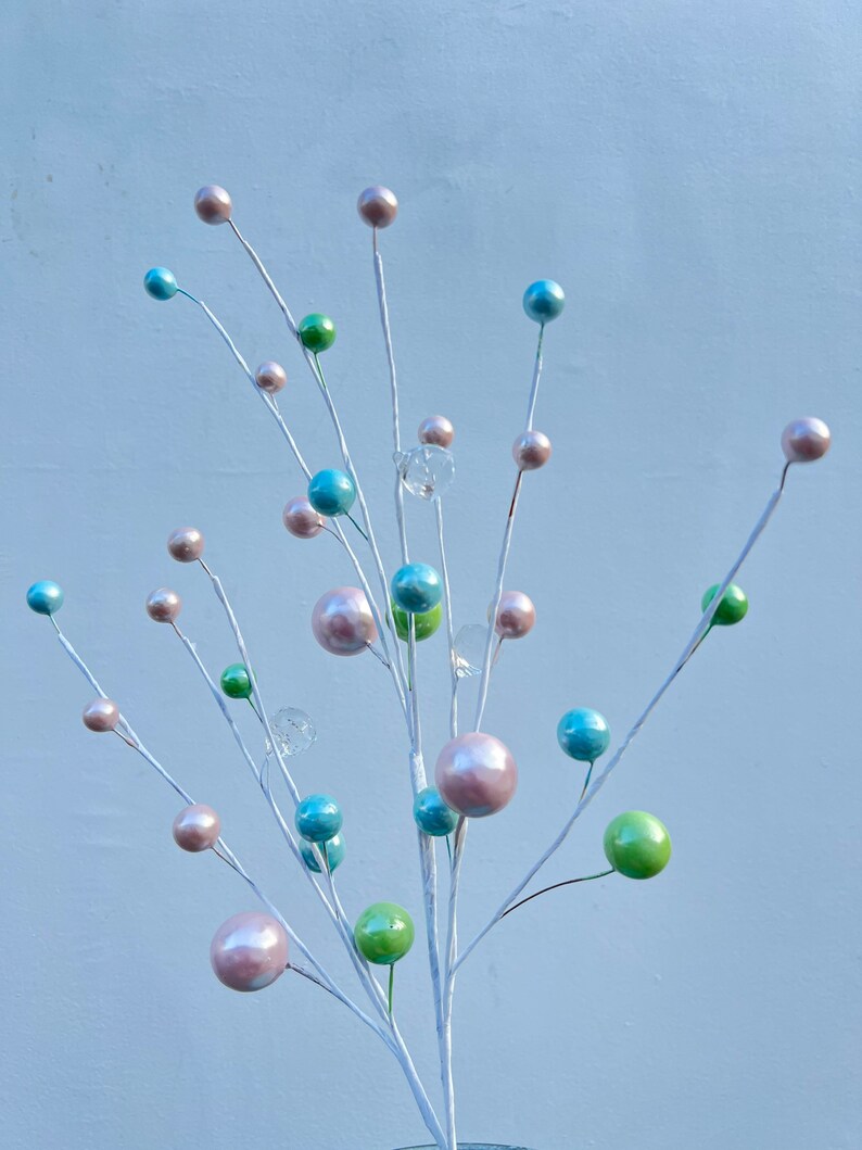 May include: A white twig spray with pastel coloured ornaments. The ornaments are in shades of pink, blue, and green. The twig spray is perfect for adding a touch of colour and whimsy to any room.