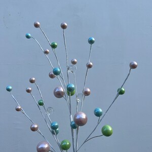 May include: A white twig spray with multiple round ornaments in shades of pink, blue, and green. The ornaments are clustered together on the twig branches.