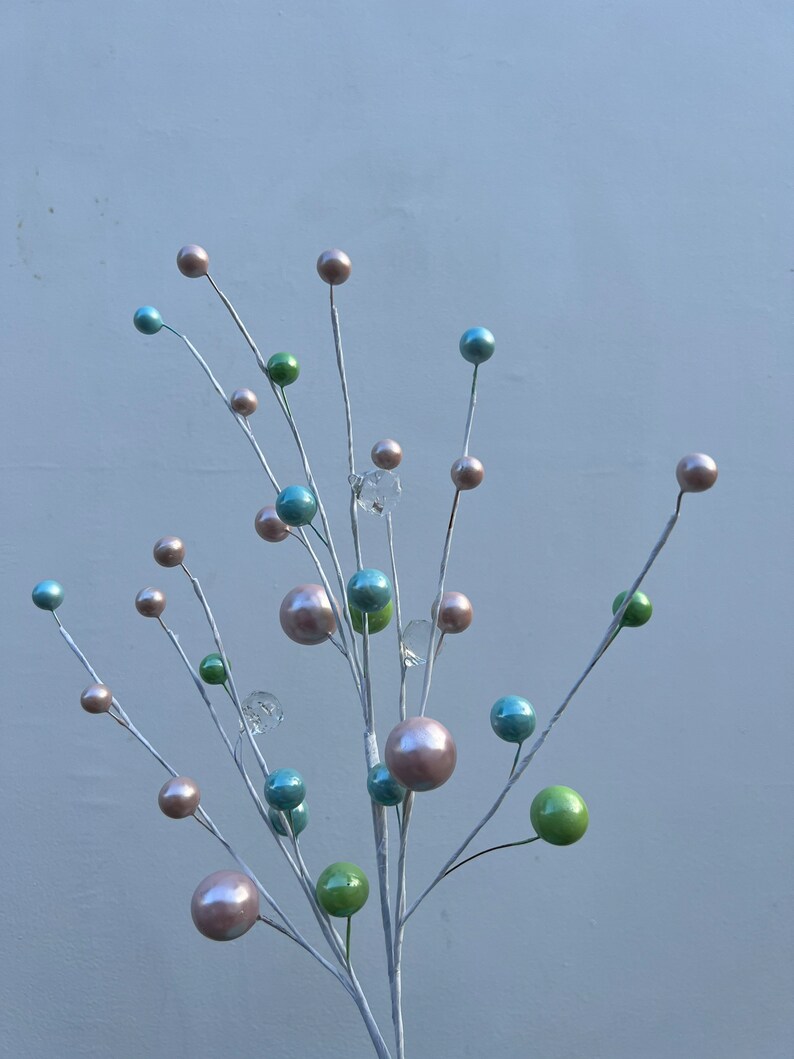 May include: A white twig spray with multiple round ornaments in shades of pink, blue, and green. The ornaments are clustered together on the twig branches.