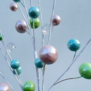 May include: A white twig branch with multiple pastel coloured ornaments. The ornaments are in shades of green, blue, and pink. Some of the ornaments are clear glass.