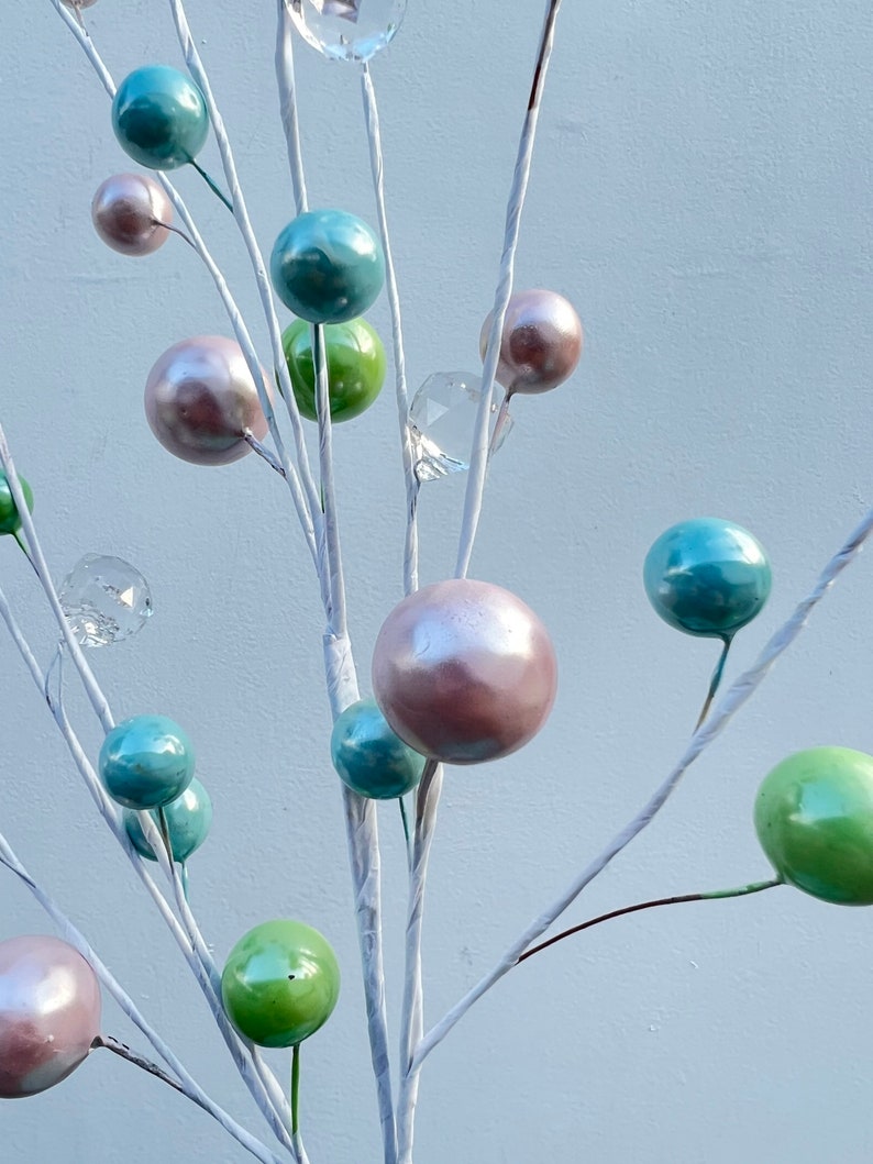 May include: A white twig branch with multiple pastel coloured ornaments. The ornaments are in shades of green, blue, and pink. Some of the ornaments are clear glass.