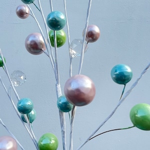 May include: A white twig branch with multiple pastel coloured ornaments. The ornaments are in shades of green, blue, and pink. Some of the ornaments are clear glass.