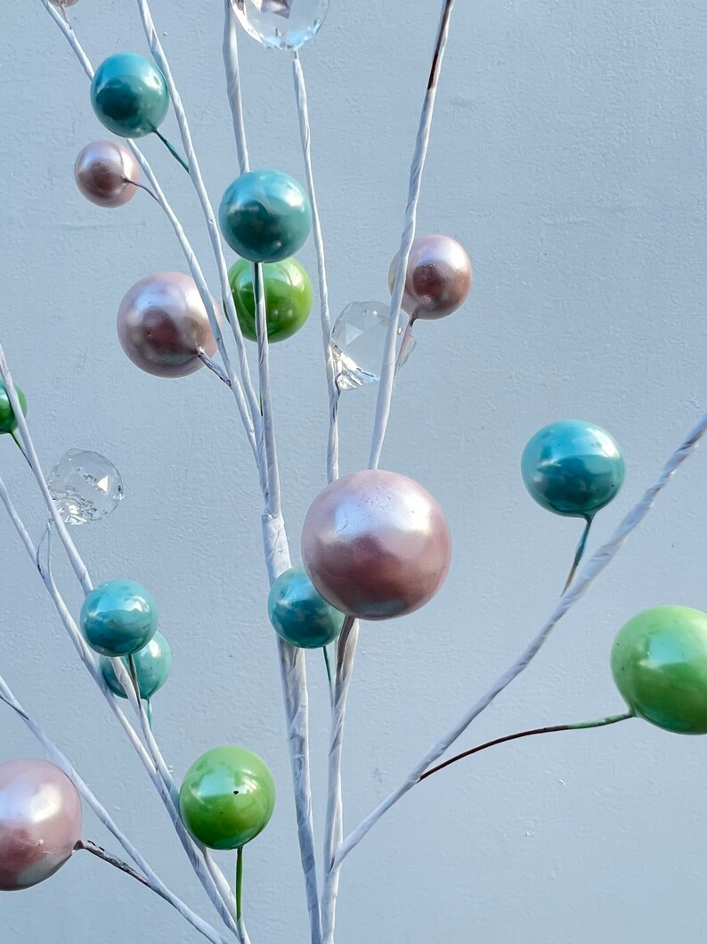 May include: A white twig branch with multiple pastel coloured ornaments. The ornaments are in shades of green, blue, and pink. Some of the ornaments are clear glass.