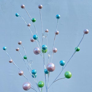 May include: A white twig spray with pastel coloured ornaments. The ornaments are in shades of pink, blue, and green. The twig spray is perfect for adding a touch of colour and whimsy to any space.