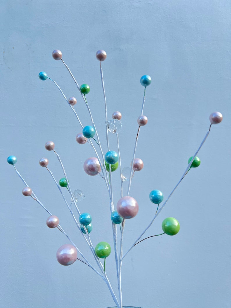 May include: A white twig spray with pastel coloured ornaments. The ornaments are in shades of pink, blue, and green. The twig spray is perfect for adding a touch of colour and whimsy to any space.
