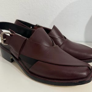 May include: Burgundy leather sandals with a square toe and ankle strap. The sandals have a low heel and a cut-out design. The sandals are approximately 2.5 cm in heel height.