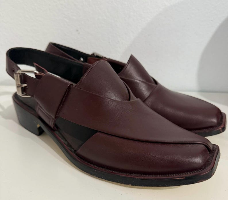 May include: Burgundy leather sandals with a square toe and ankle strap. The sandals have a low heel and a cut-out design. The sandals are approximately 2.5 cm in heel height.