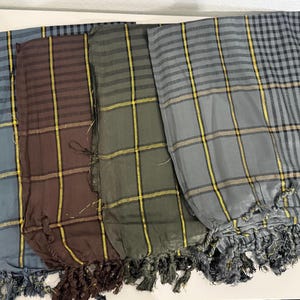 May include: A collection of five plaid scarves in various colors, including blue, brown, and gray. Each scarf features a fringed edge and a grid pattern with yellow accents. The scarves are neatly arranged, showcasing their different color combinations.