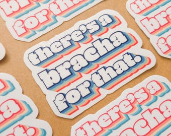 Könnte beinhalten: Mehrere Aufkleber mit dem Text "there's a bracha for that" in einem Retro-Schriftstil. Der Text ist weiß mit blauen, roten und gelben Umrissen. Die Aufkleber liegen auf einer hellbraunen Oberfläche.