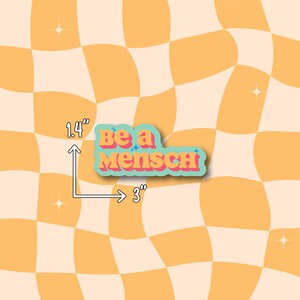 K&ouml;nnte beinhalten: Ein Aufkleber mit dem Text "Be a Mensch" in einer Retro-Schriftart, der 7,6 cm breit und 3,6 cm hoch ist. Der Aufkleber hat einen tealfarbenen Umriss mit einem Pfirsich- und Blauton, vor einem wellenf&ouml;rmigen, karierten orange-cremefarbenen Hintergrund.