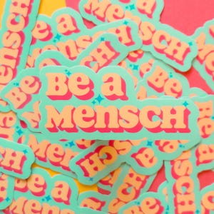 K&ouml;nnte beinhalten: Eine Ansammlung von Aufklebern mit dem Schriftzug "Be a Mensch" in Orange, umrandet in Rot, auf hellgr&uuml;nem Hintergrund. Die Aufkleber haben eine Retro-Schriftart und sind auf einem bunten Hintergrund verteilt.
