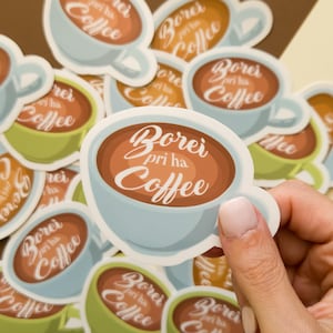May include: A collection of coffee-themed stickers. Each sticker features a light blue coffee cup with a brown coffee fill and the text "Borei pri ha Coffee" in white script. Other stickers are green and orange.