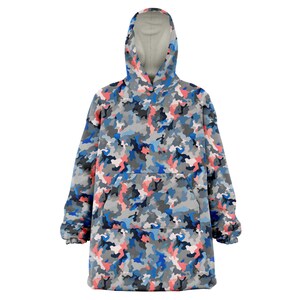 Puede incluir: Una manta con capucha con un patr&oacute;n de camuflaje azul, gris y rosa. La manta tiene un bolsillo grande en la parte delantera y una capucha con cord&oacute;n.